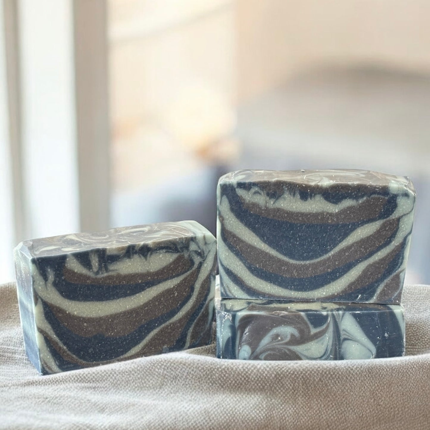 Two marbled soap bars(dark blue, light blue and brown)on a textured surface with a blurred background