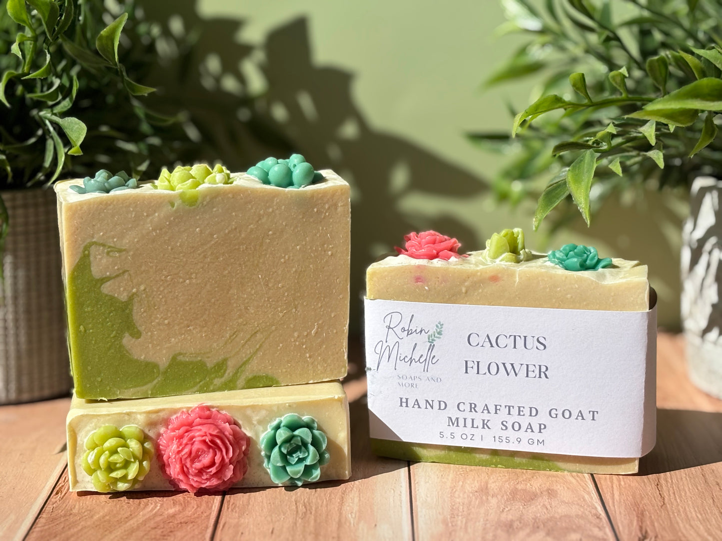 Handcrafted goat milk soap with cactus and flower designs on a wooden surface with plants in the background.