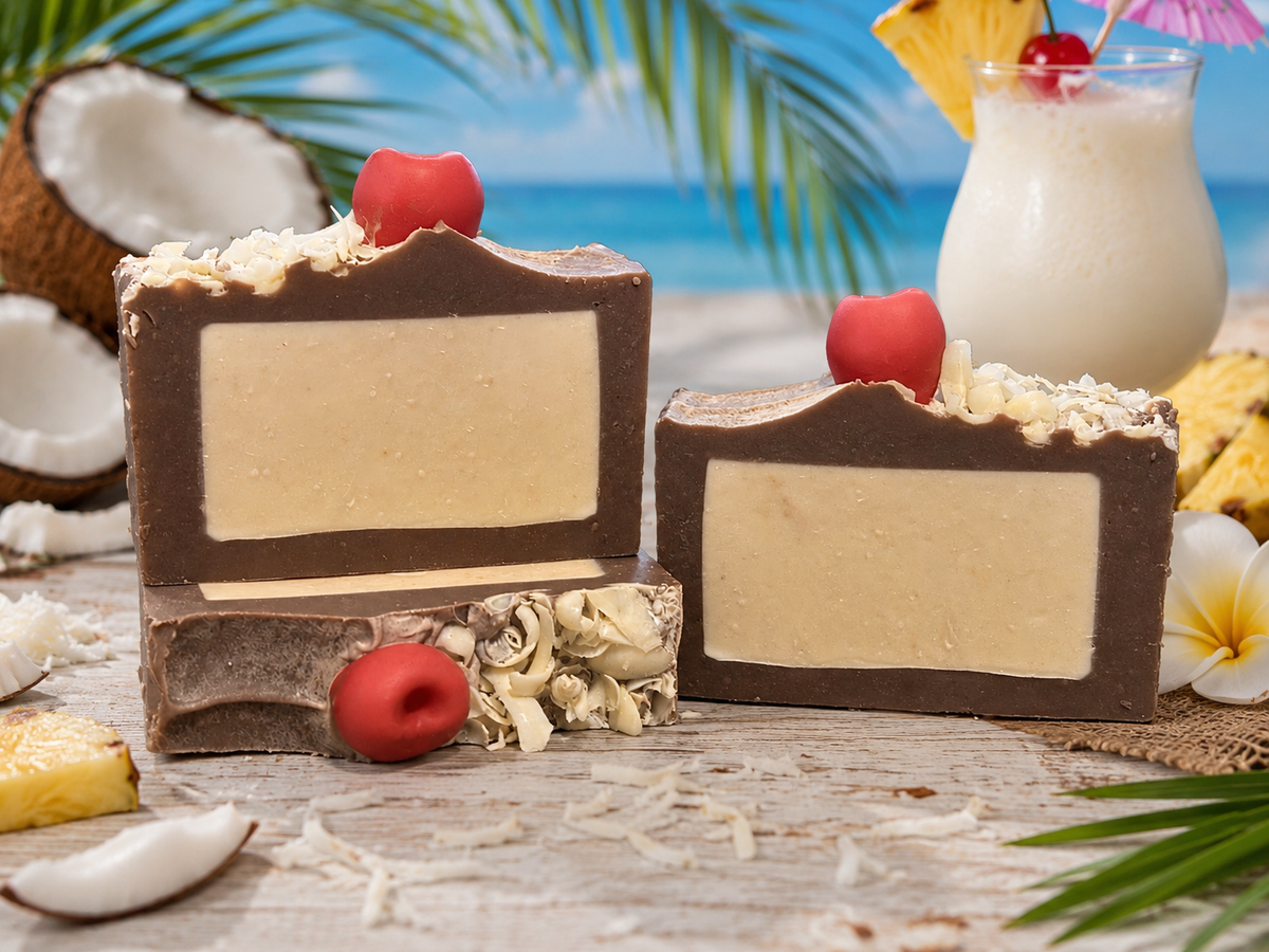 Three rectangular bars of brown soap with cream-colored centers, decorated with red cherries and shredded coconut, displayed on a tropical beach-themed surface with coconuts, pineapple, and a tiki drink in the background.
