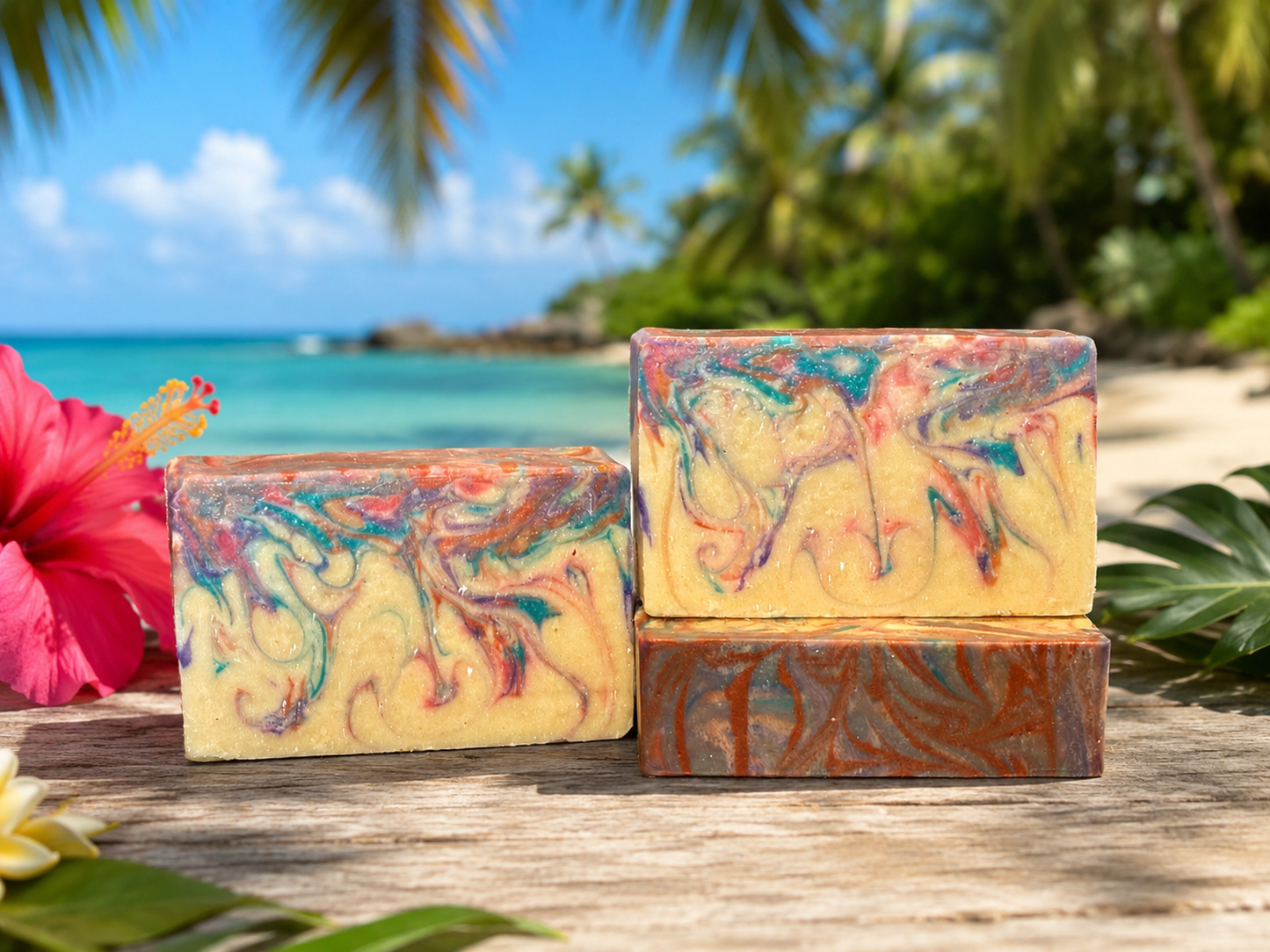 Three marbled artisan soap bars with swirls of yellow, orange, red, and teal, displayed on a rustic wooden table with a tropical beach and palm tree background.
