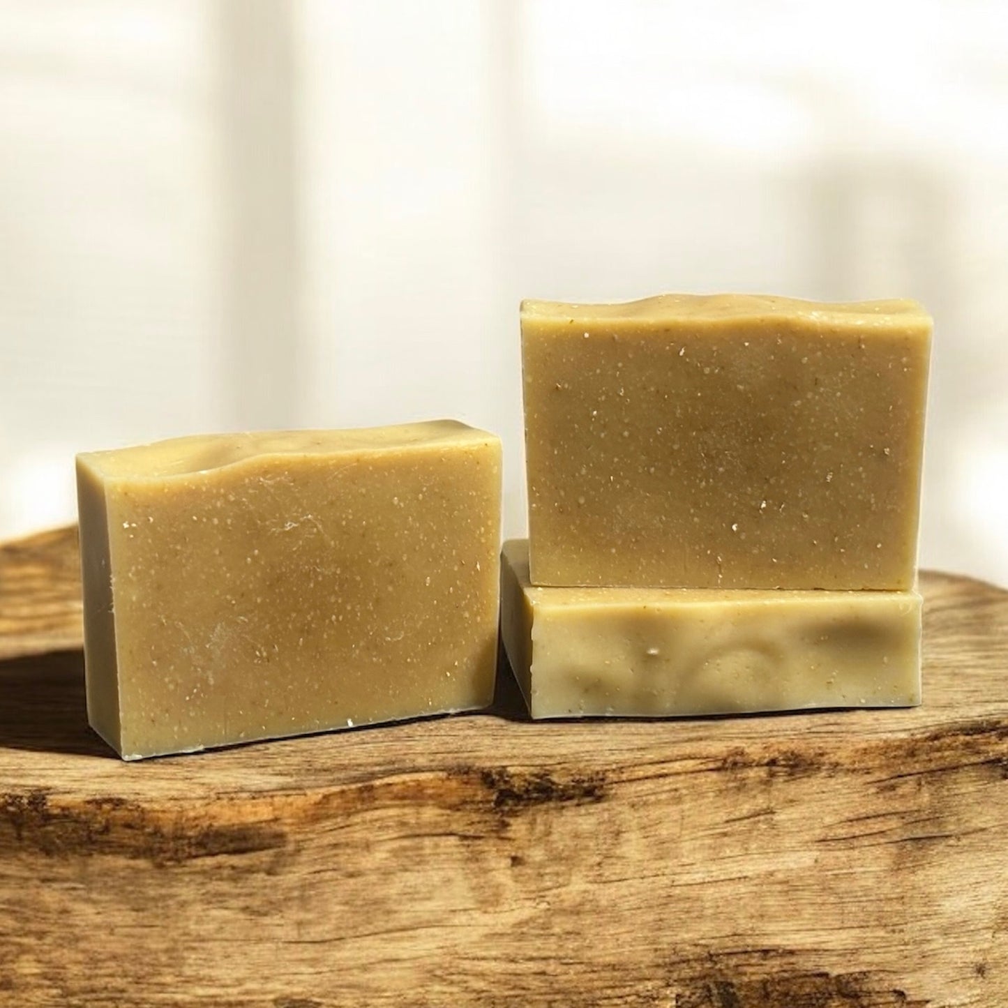 Three bars of unscented oatmeal and honey goat milk soap on a wooden surface with a neutral background.