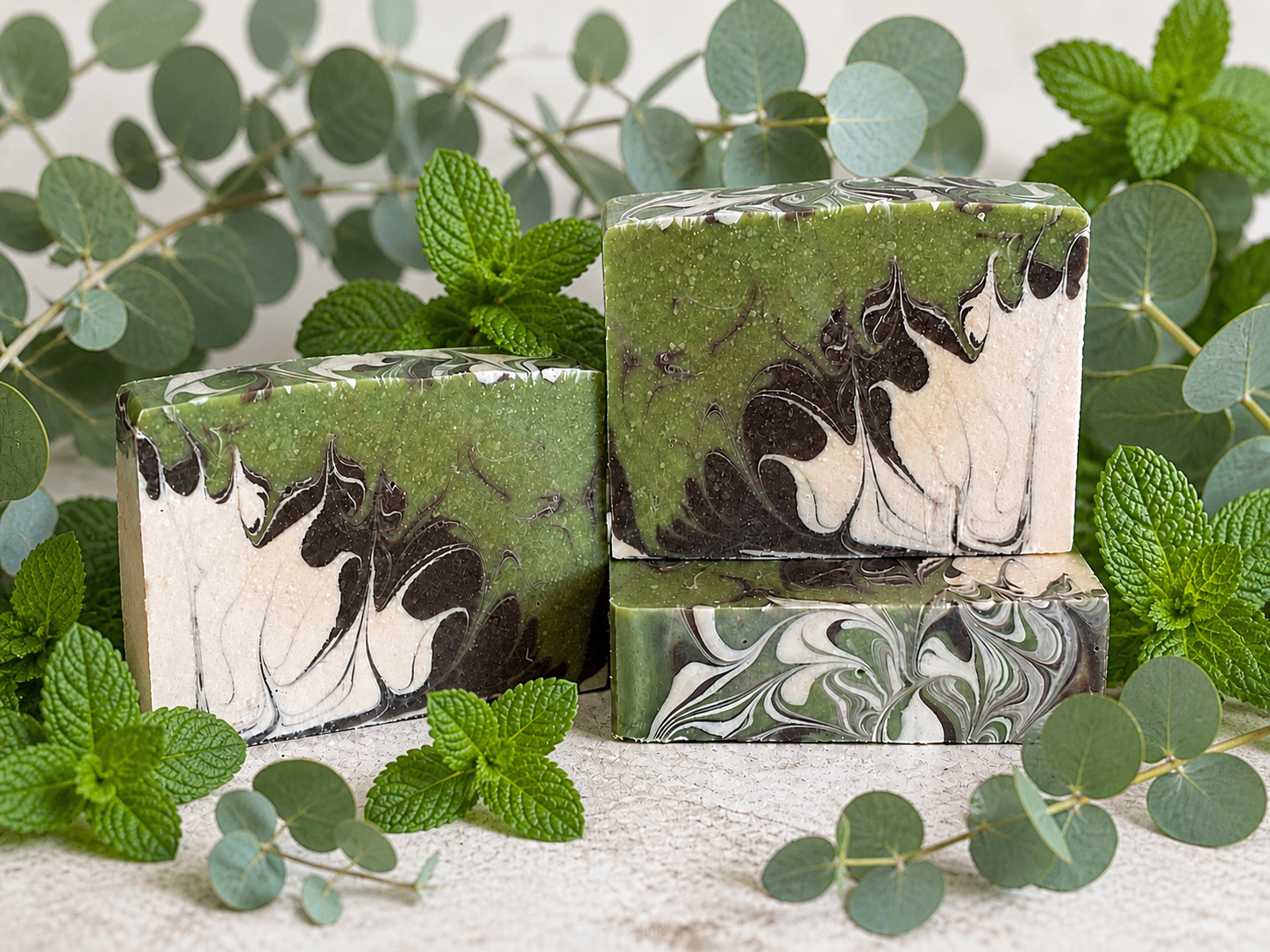 Marbled green and white soap bars with brown abstract designs, surrounded by green leaves on a light background.