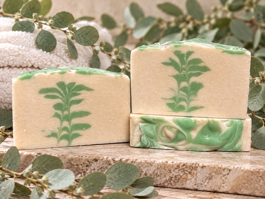 Three white and green soaps with leaf designs on a marble top with eucalyptus 