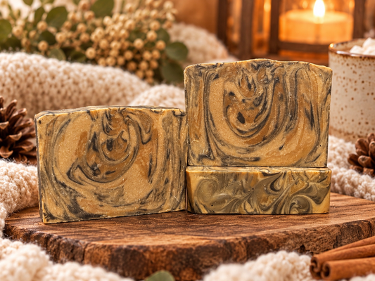 Three marbled soaps on a wooden slab with blankets and pinecones.