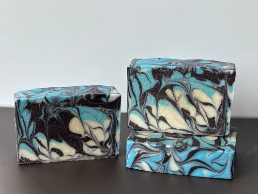 Marbled soap bars with blue, black, and white patterns on a dark surface.