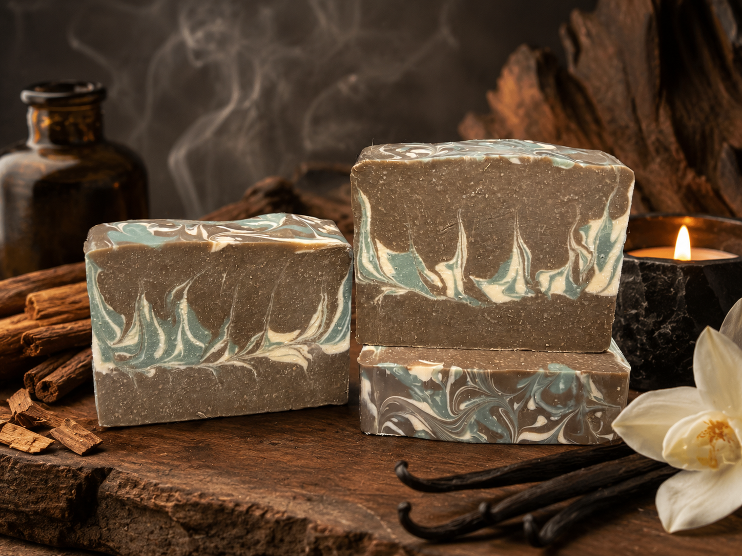 Three bars of marbled soap on a wooden surface with vanilla beans and a candle.