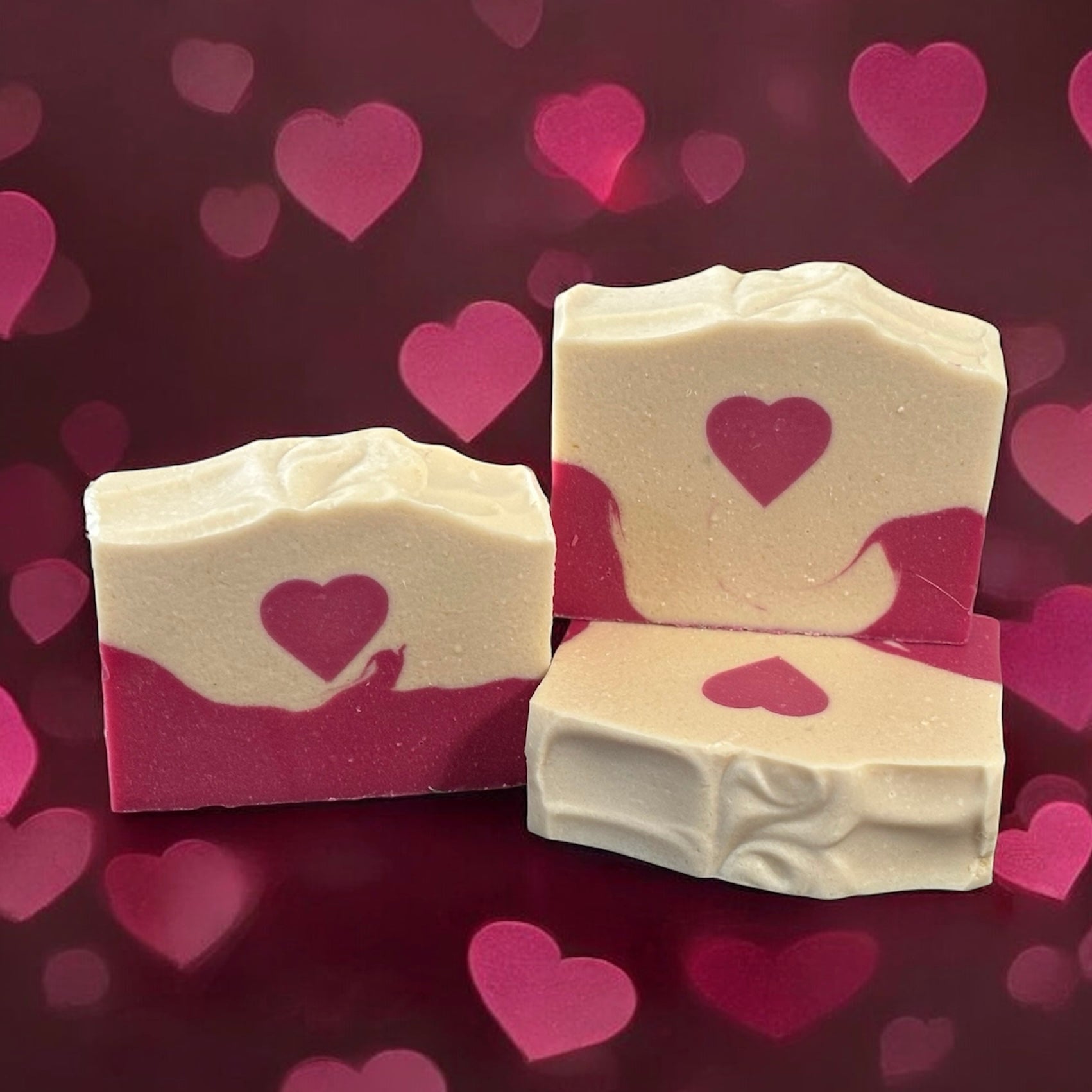 Three bars of soap with heart designs on a pink heart-patterned background