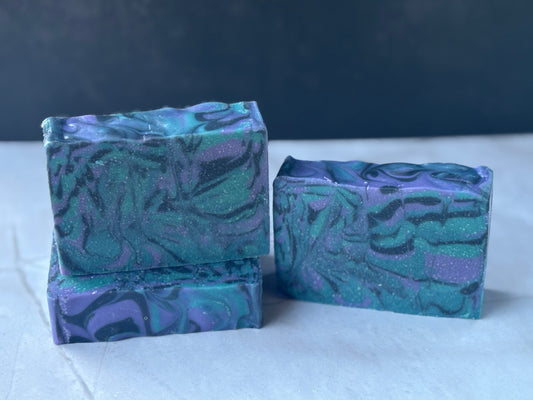 Three bars of blue, black and purple soap with a wavy pattern on a white surface.