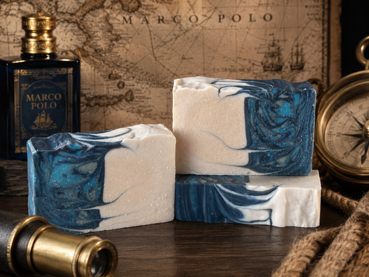 Two bars of soap with blue and white swirls on a wooden surface, with a Marco Polo bottle and map in the background.
